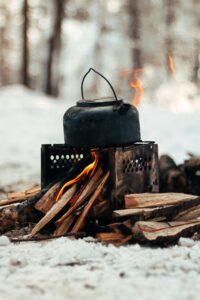 A kettle on a campfire brings warmth to a snowy winter forest scene.