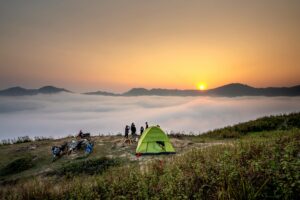 Capture of a serene camping scene at sunrise with a view over a sea of clouds and mountains.